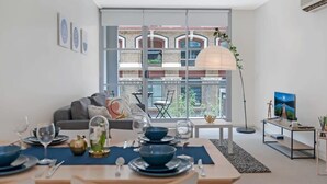 Un salon moderne avec un coin repas, de grandes fenêtres et une vue sur un immeuble à la façade en briques.