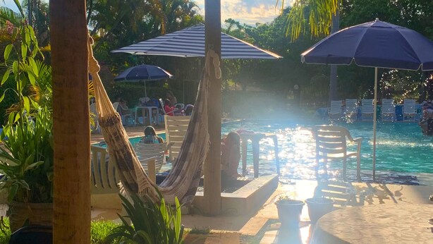 Zona de piscina con una hamaca, sillones de descanso y sombrillas.