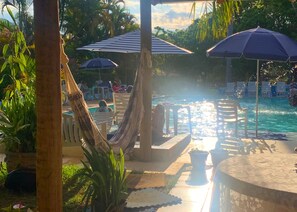 A poolside area with a hammock, lounge chairs, and umbrellas.