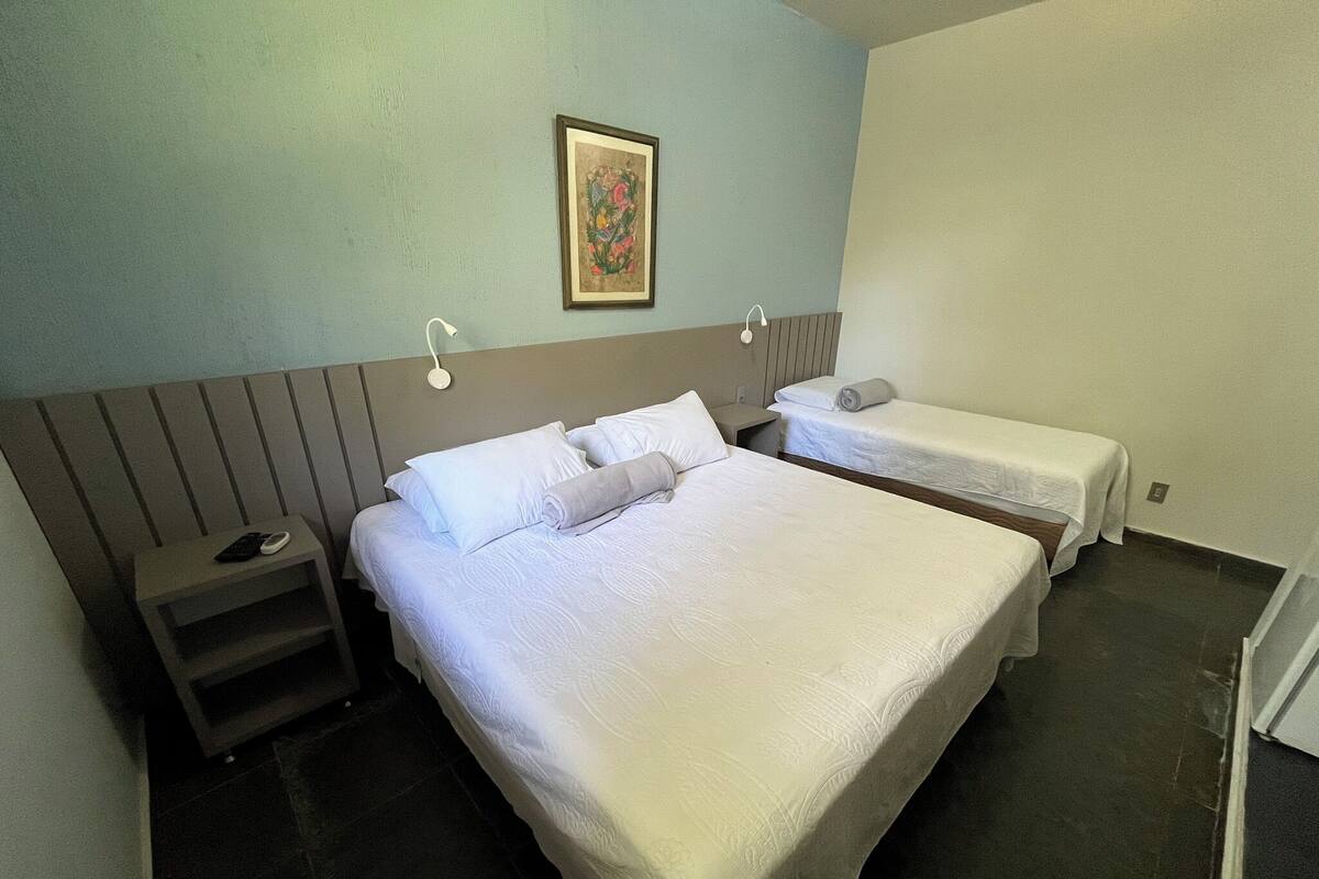 Habitación de hotel con dos camas, una mesita de noche, una pequeña mesa y un cuadro colgado en la pared.