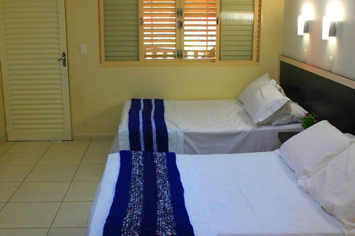 Habitación de hotel con dos camas, una ventana con persianas, una puerta y una lámpara fijada a la pared.