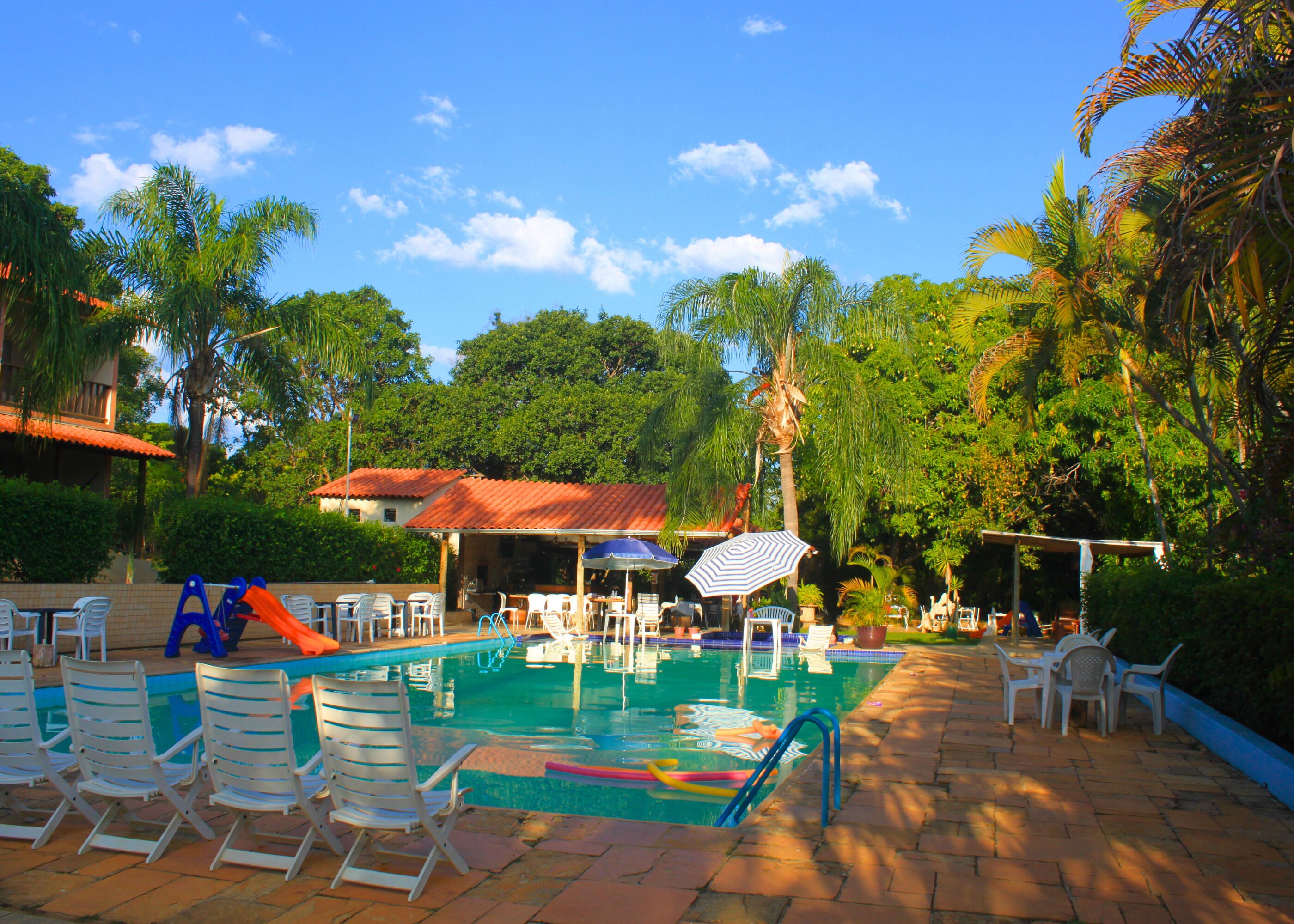A pool area with lounge chairs, umbrellas, and a building with a red roof.