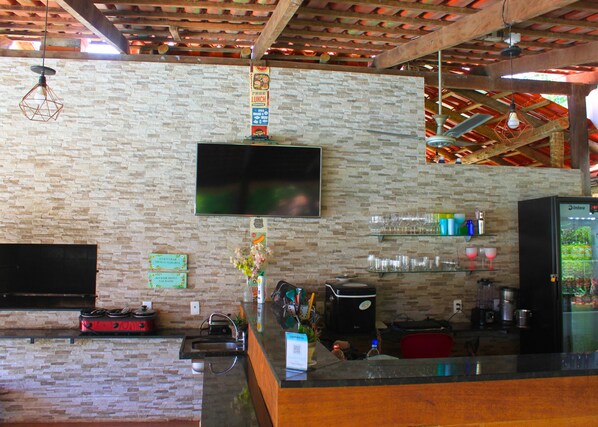 A bar area with a stone wall, a flat-screen TV, a refrigerator, and various bar items.