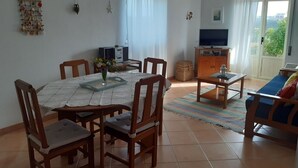 Een eetruimte met een ronde tafel, stoelen en een televisie op de achtergrond.