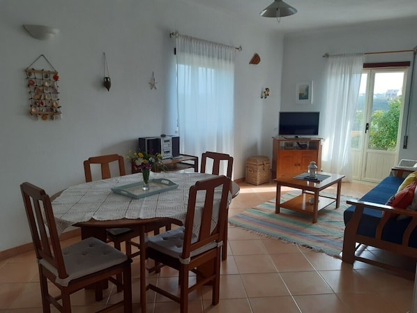 A dining area with a round table, chairs, and a TV in the background.