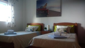 Een hotelkamer met twee eenpersoonsbedden, elk met een houten hoofdbord, witte linnens en een groen kussen. Daarboven hangt een schilderij van een auto aan de muur.