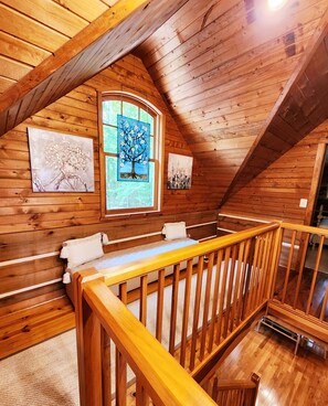Cozy attic bedroom with a small bed, wall-mounted paintings, and a balcony with a stained glass window.