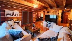 Interior acogedor de una cabaña de madera con techo de madera, un televisor grande y una chimenea.
