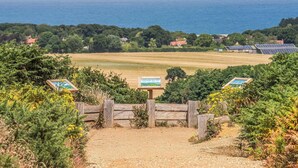 Un paysage côtier avec des éoliennes, des panneaux solaires et une clôture en bois qui mène à un sentier.