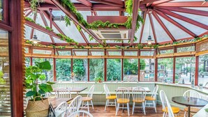 Un espace extérieur aménagé avec des tables et des chaises en bois, entouré de grandes fenêtres et surmonté d’un toit en métal.