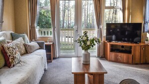 Un salon confortable avec un canapé, une table basse, un téléviseur et une grande fenêtre agrémentée de rideaux.