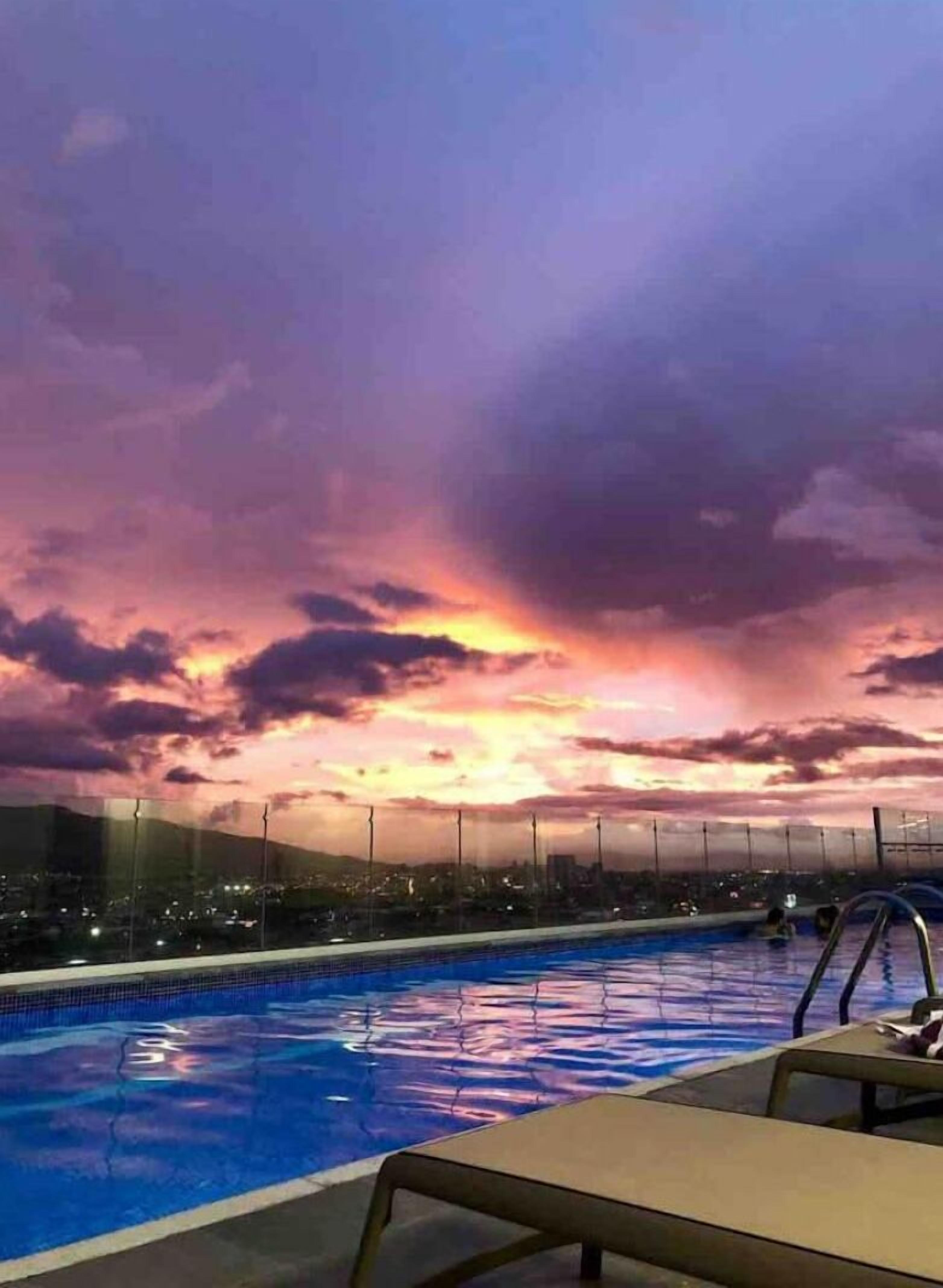 A swimming pool with a view of a cityscape during sunset.