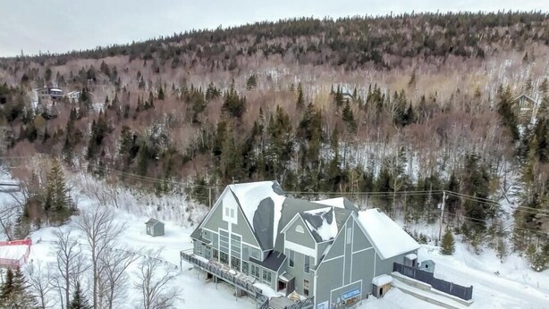 Un edificio grande de dos pisos con techo nevado, rodeado de un área boscosa.