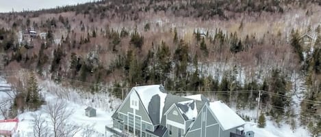Un edificio grande de dos pisos con techo nevado, rodeado de un área boscosa.