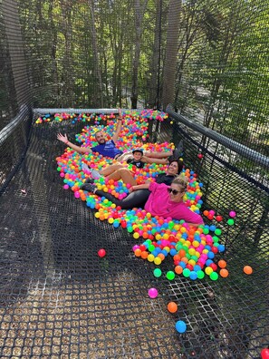 Un groupe de personnes est allongé dans une fosse remplie de balles colorées, le tout étant entouré d’une structure en filet.