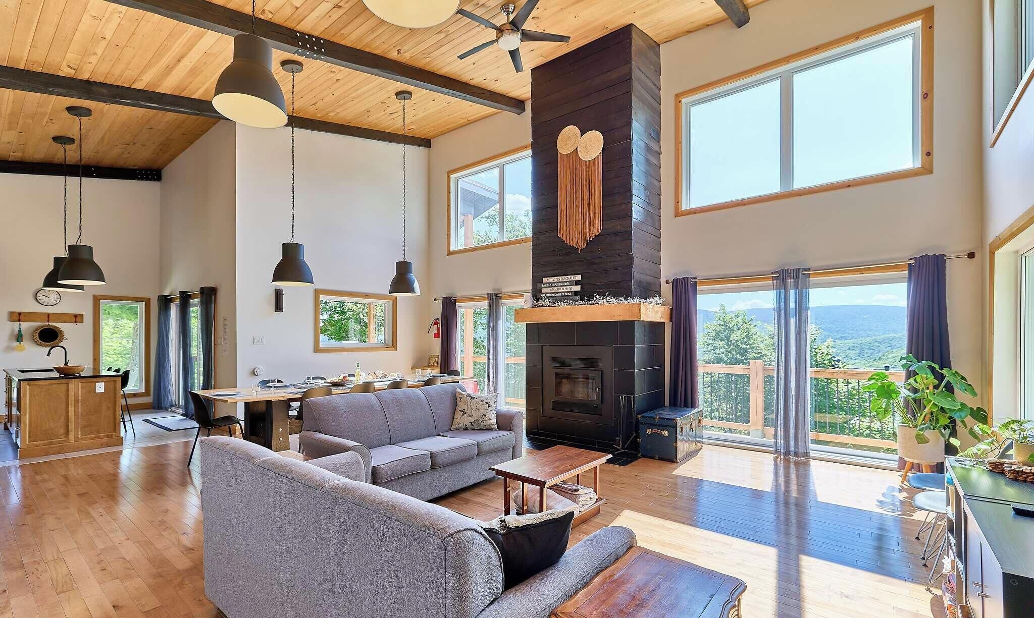 A spacious living area with a fireplace, large windows, and a high ceiling.