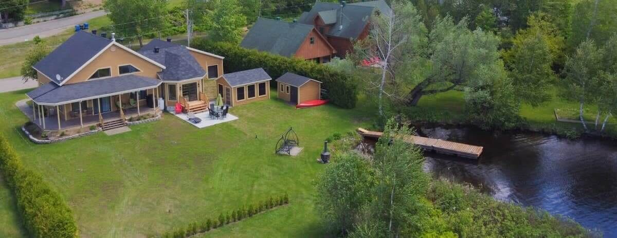 A large house with a covered porch, a small shed, and a dock over a river.