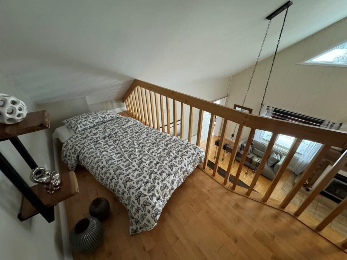 Un dormitori amb un llit, sòl de fusta i una escala que condueix a un nivell superior.