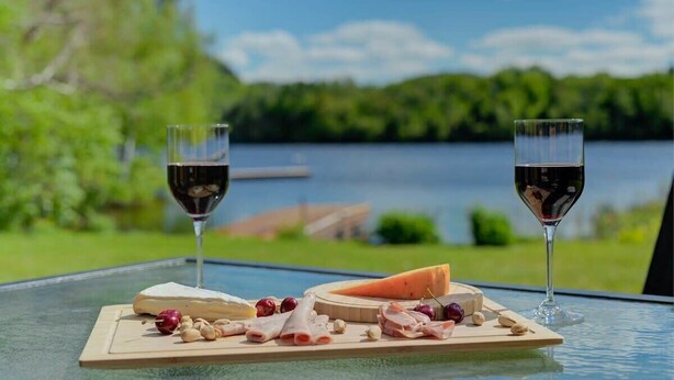 Een tafel met een kaasplank, twee glazen rode wijn en een prachtig uitzicht op een meer.