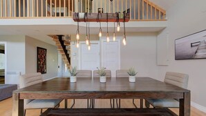 Een ruime eetruimte met een grote houten tafel, meerdere stoelen en hangende lampen.