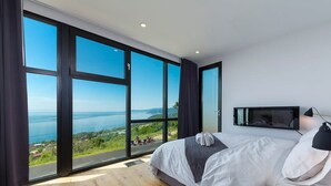 A bedroom with a large bed, a TV, and a view of the sea. - L’Eaurizon | Private Spa & St. Lawrence View (La Malbaie)