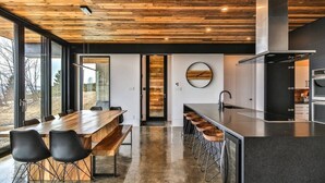 A modern kitchen with a wooden ceiling, a large island with bar stools, and a view through large windows. - L’Eaurizon | Private Spa & St. Lawrence View (La Malbaie)
