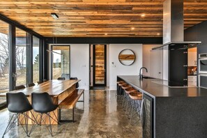 Une cuisine moderne avec un plafond en bois, un grand îlot central doté de tabourets de bar et une vue dégagée grâce à de grandes fenêtres.