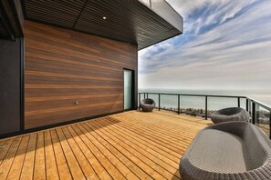 A modern deck with wooden flooring, a glass railing, and a view of the sea.