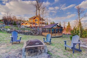 A large house with a deck, a fire pit, and Adirondack chairs.