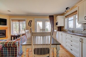 Un coin repas comprenant une table en bois, des chaises blanches, un canapé et une cuisine avec des meubles blancs et un four à micro-ondes.