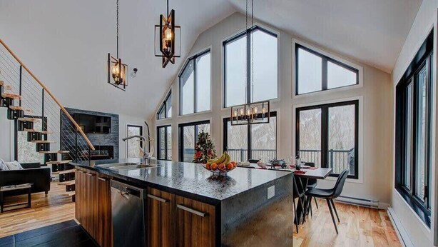 A modern kitchen with a large island, wooden flooring, and large windows.