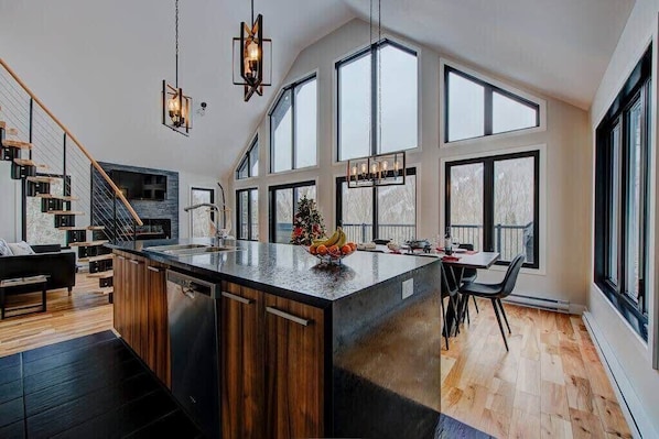 A modern kitchen with a large island, wooden flooring, and large windows.