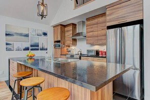 Une cuisine moderne dotée d’un grand îlot central, de meubles en bois, d’appareils électroménagers en acier inoxydable et d’un luminaire suspendu.