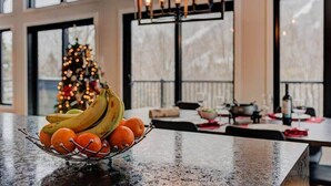 A kitchen counter with a fruit bowl, a Christmas tree, and a dining area with a chandelier.
