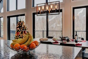A kitchen counter with a fruit bowl, a Christmas tree, and a dining area with a chandelier.