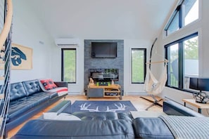 Un salon moderne avec un canapé, un téléviseur à écran plat fixé à un mur en pierre, un hamac et de grandes fenêtres.