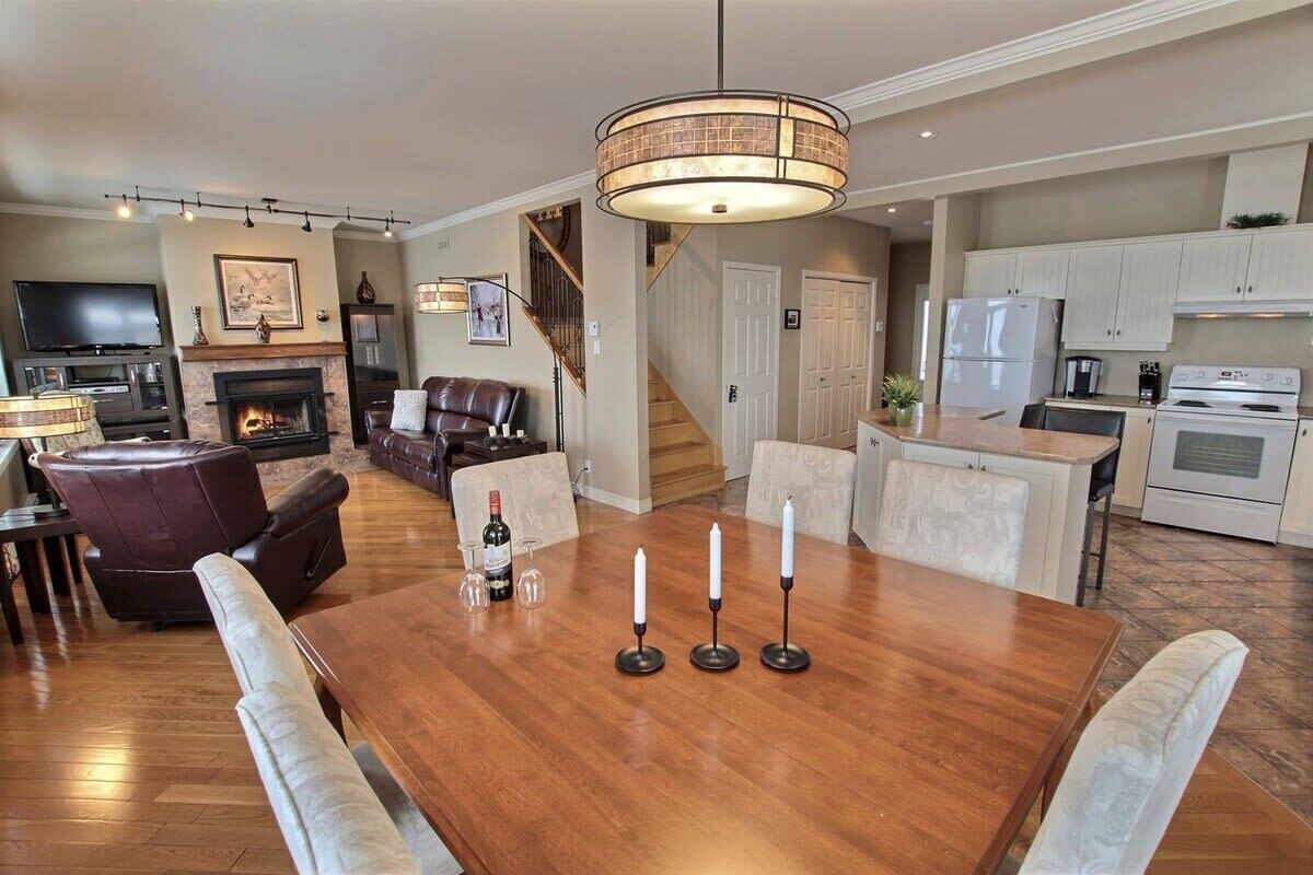 Amplia sala de estar con mesa de comedor de madera, asientos cómodos, chimenea y una zona de cocina al fondo.