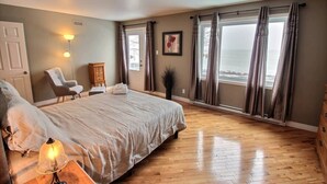 Une chambre avec un grand lit, une chaise, une commode et une fenêtre avec des rideaux.