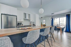 A modern kitchen with a central island, bar stools, and a dining area with a view. - Le Baikal | Nature, Trails & EV Charger (Pont-Rouge)