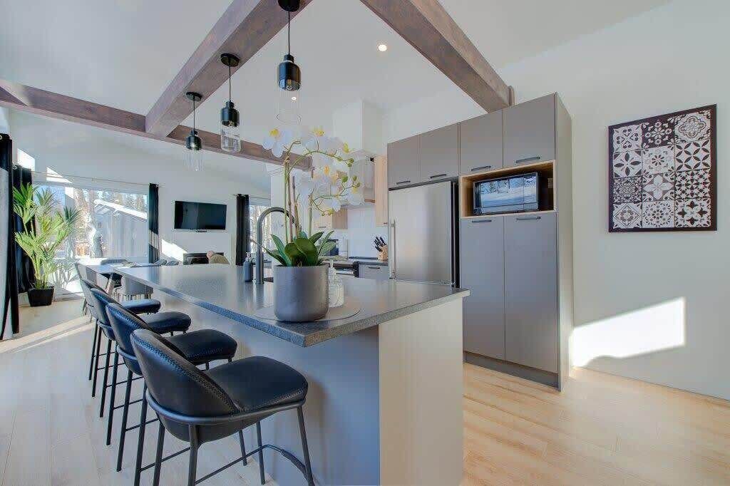 A modern kitchen with a central island, bar stools, a large refrigerator, and a flat-screen TV.