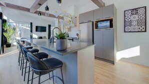 A modern kitchen with a central island, bar stools, a large refrigerator, and a flat-screen TV.