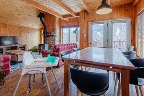 A wooden cabin interior with a dining table, chairs, a television, a fireplace, and a sofa. - Boisé du Midi 66C | Hiking & Ski Escape (Saint-Philémon)