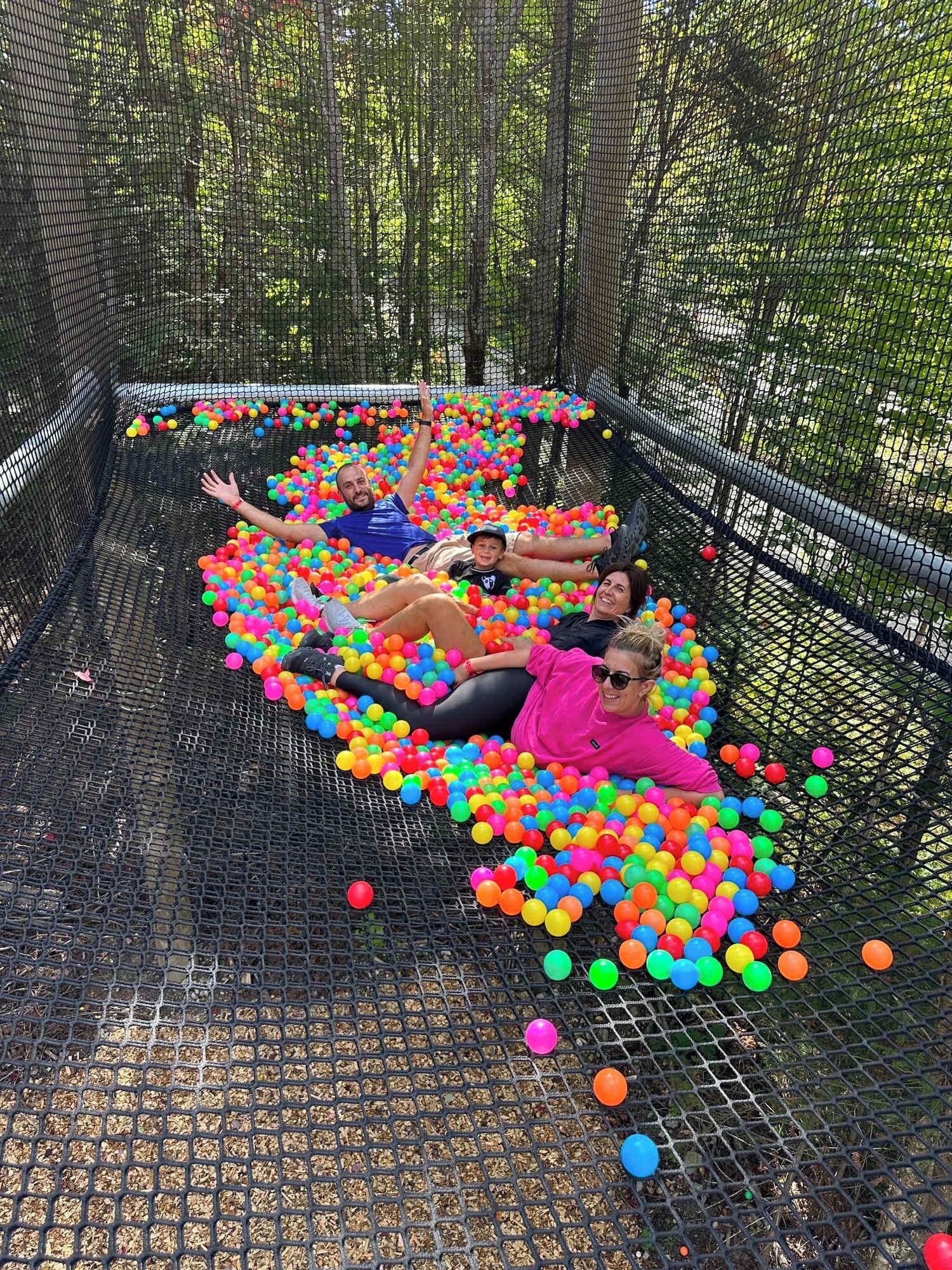 A group of people lying in a ball pit filled with colorful balls, enclosed by a netted structure.