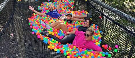 A group of people lying in a ball pit filled with colorful balls, enclosed by a netted structure.