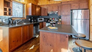 Een houten keuken in blokhutstijl met een centraal eiland, roestvrijstalen apparatuur en een raam met zonwering.