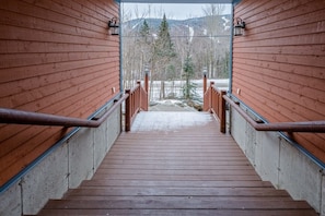 A wooden staircase leading to a deck with metal railings, surrounded by a snowy landscape and trees. - Boisé du Midi 66C | Hiking & Ski Escape (Saint-Philémon)