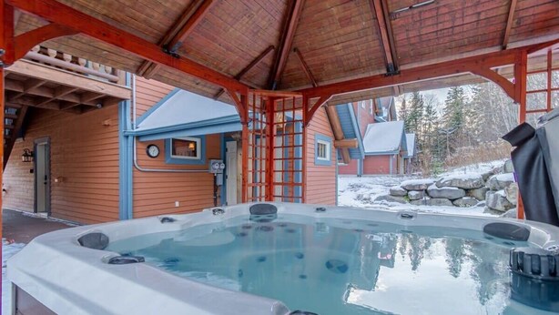 Ein Whirlpool unter einer Holzhütte mit Blick auf ein Haus und Schnee.