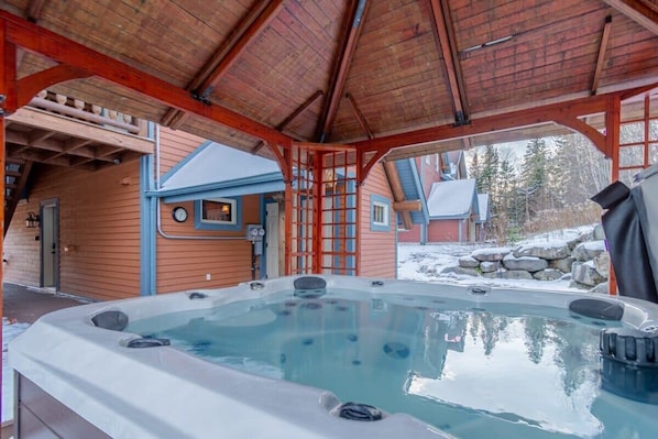 A hot tub under a wooden pavilion with a view of a house and snow outside. - Boisé du Midi 66D | Nature at Massif du Sud (Saint-Philémon)