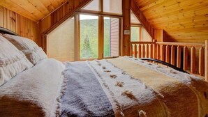 Ein Schlafzimmer einer Holzhütte mit Bett, Fenster und Blick ins Freie.