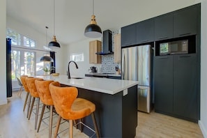 A modern kitchen with a central island, bar stools, pendant lights, and built-in appliances.
